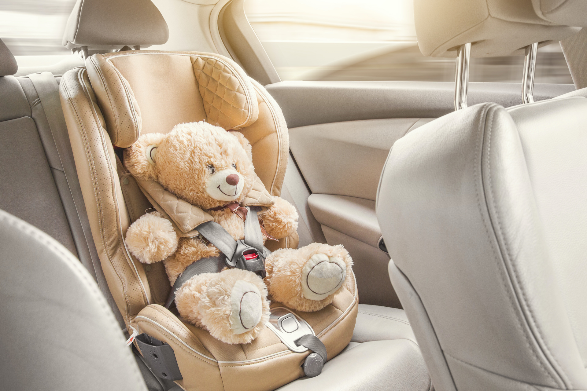 Baby child seat car. A beige teddy bear is fastened with seat belts in a car seat. Travel by car.